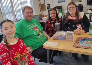 Adults and children seated at a table wearing holiday sweaters.