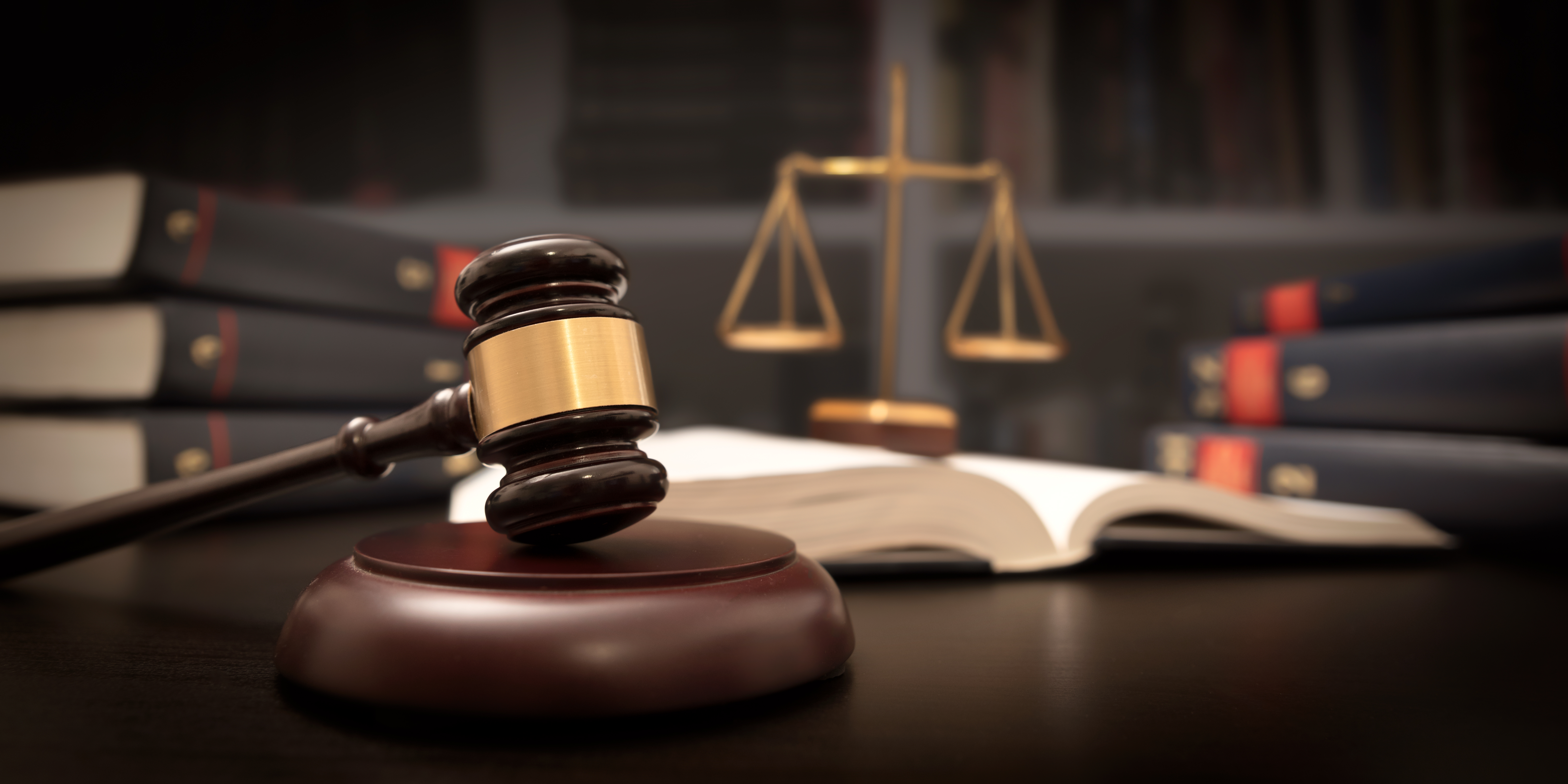 Court gavel on a strike plate, with the Scales of Justice and books in the background