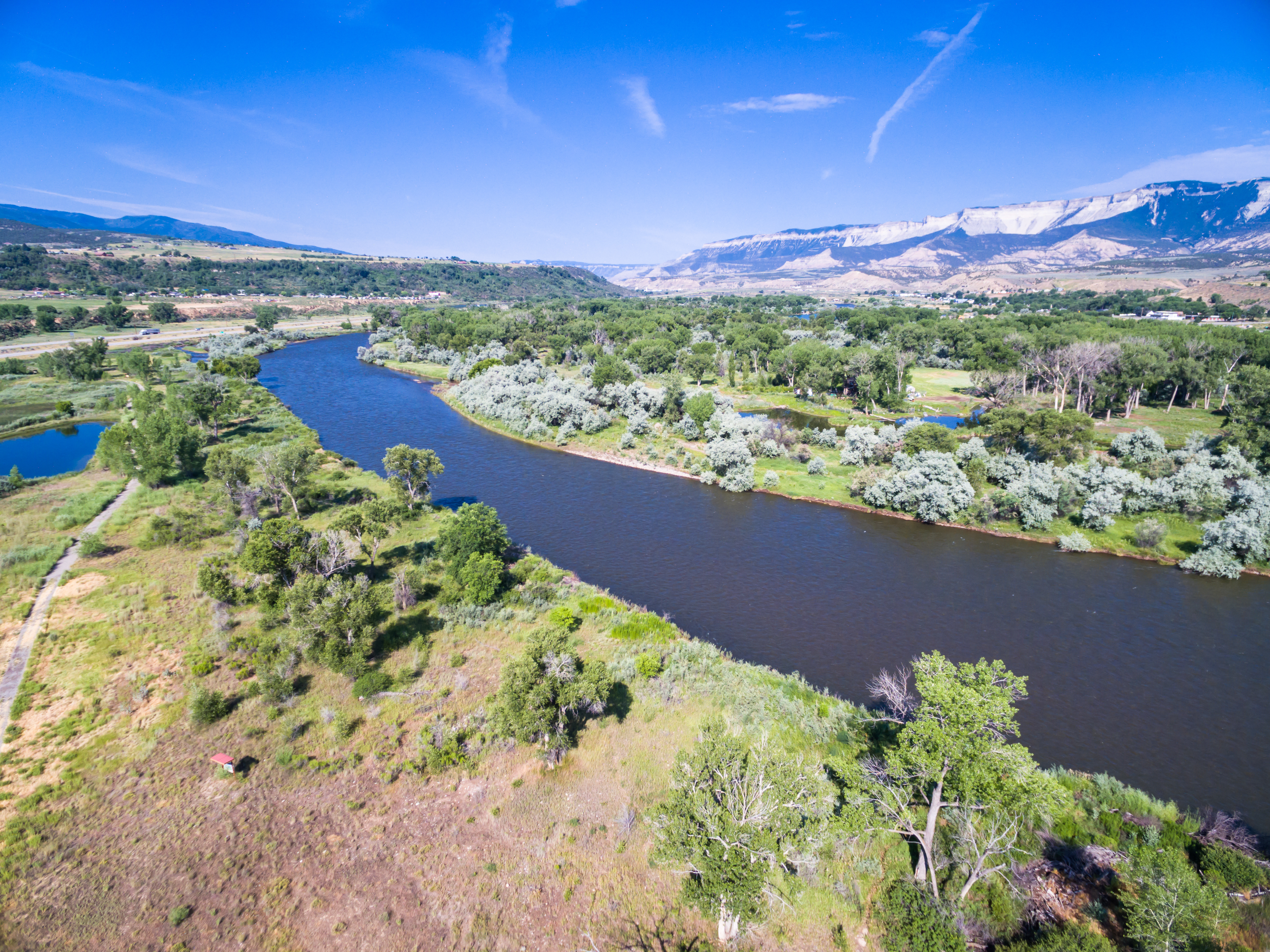 Aerial view of the Colorado River surrounded by low vegetation with mountains and blue sky in the background.