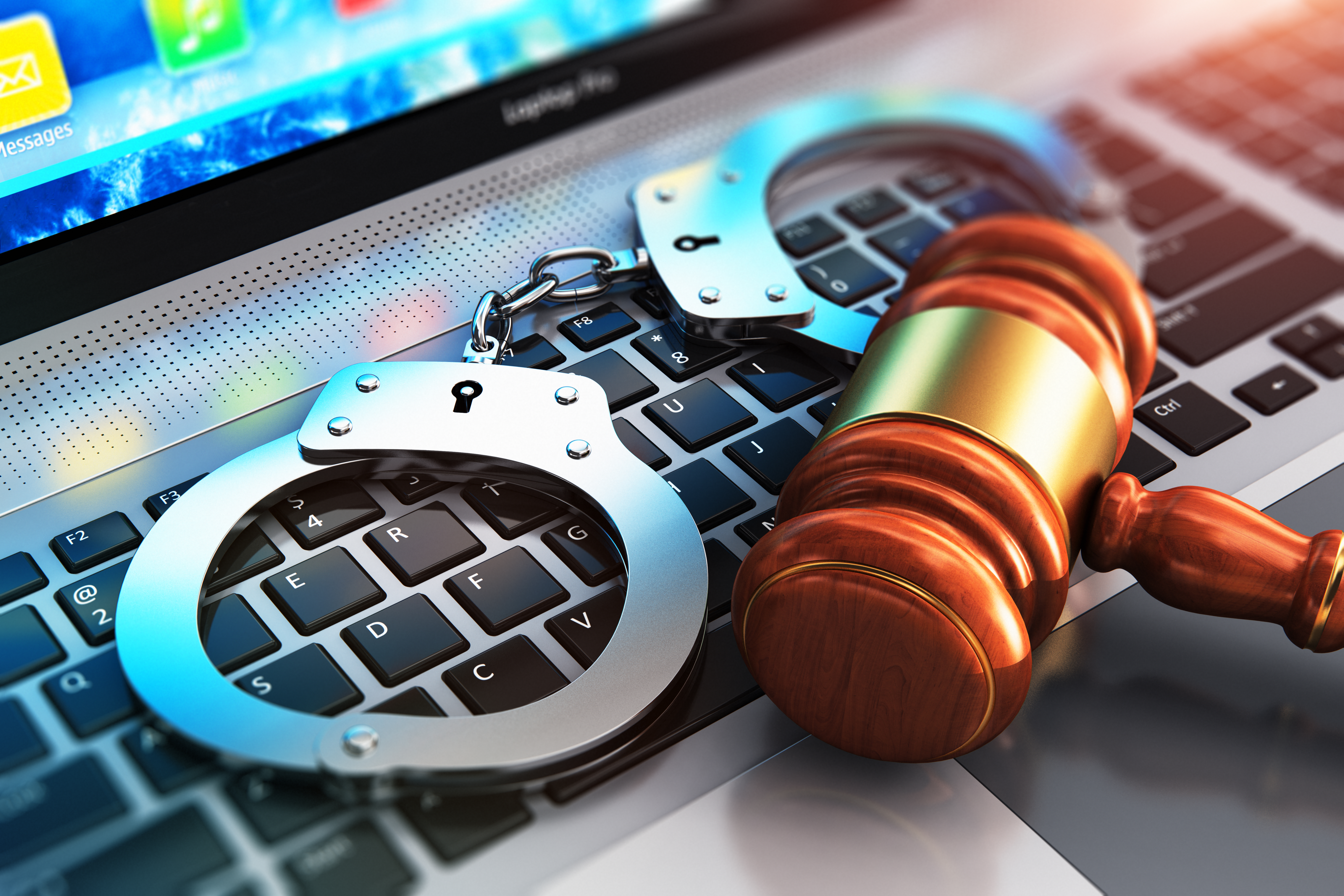 Closeup of handcuffs and court gavel on a laptop computer keyboard - scanrail - iStock-910651416