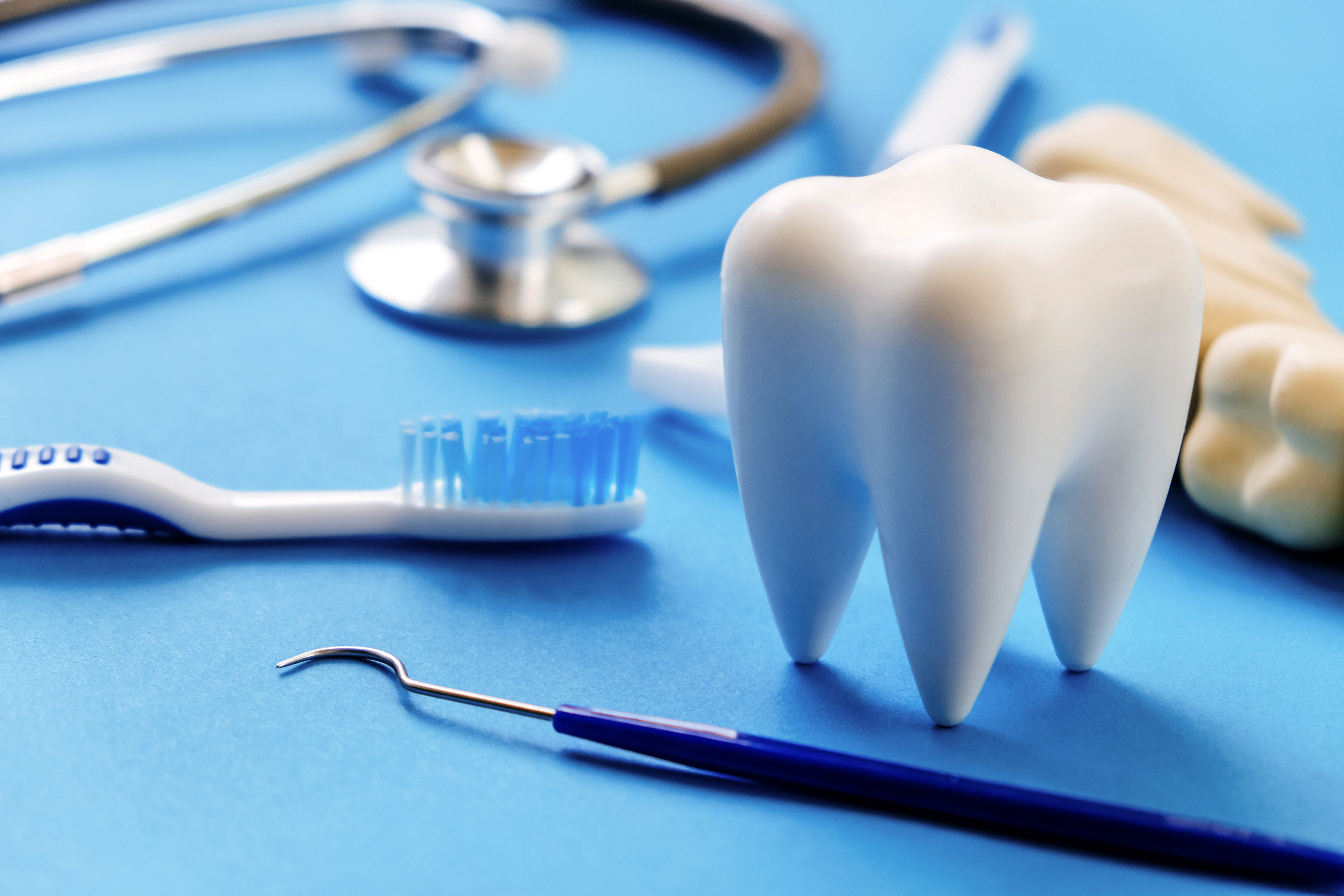 Replica human tooth surrounded by dental instruments and a stethoscope.