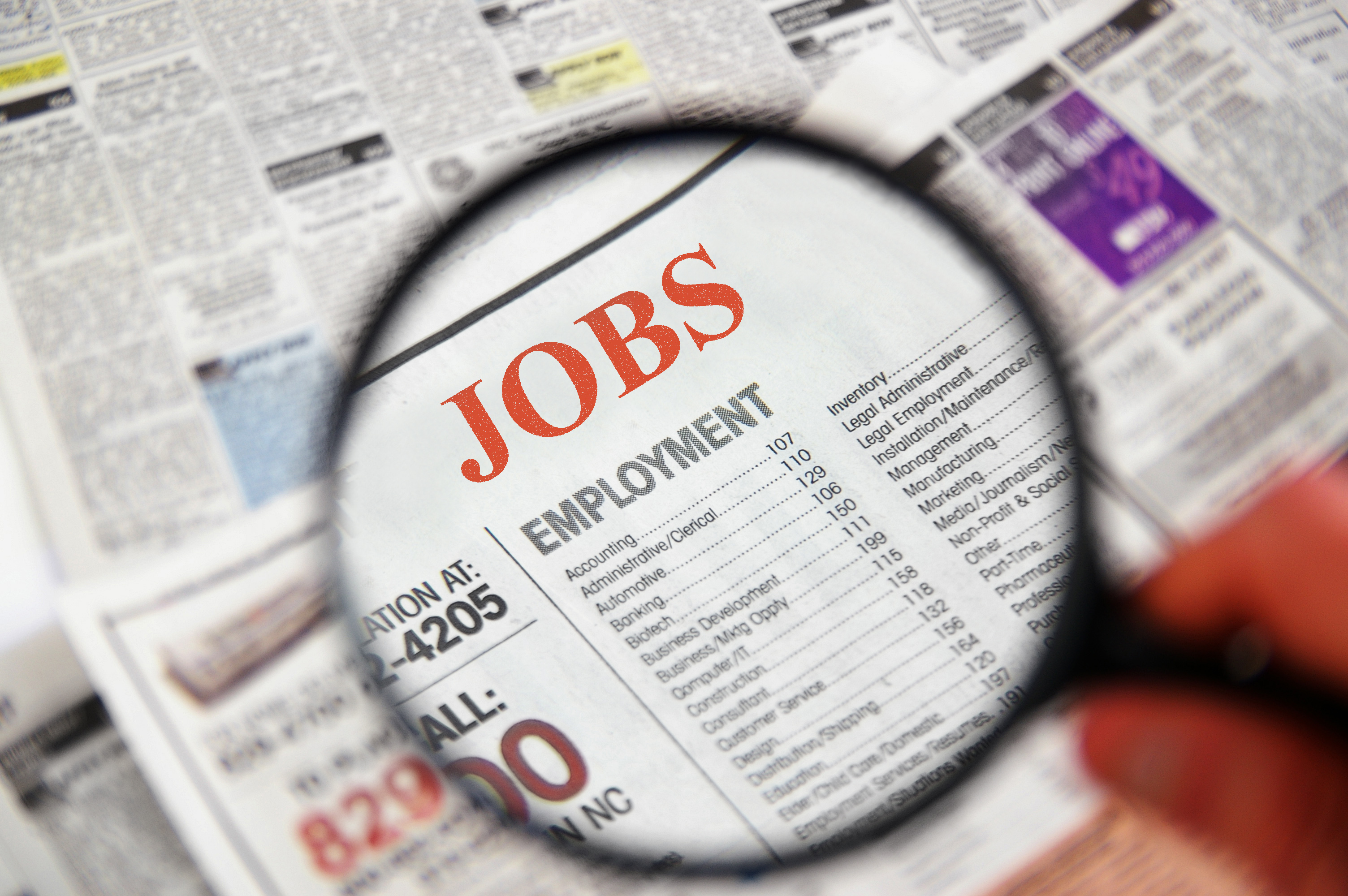 Magnifying glass over a newspaper showing the Jobs section