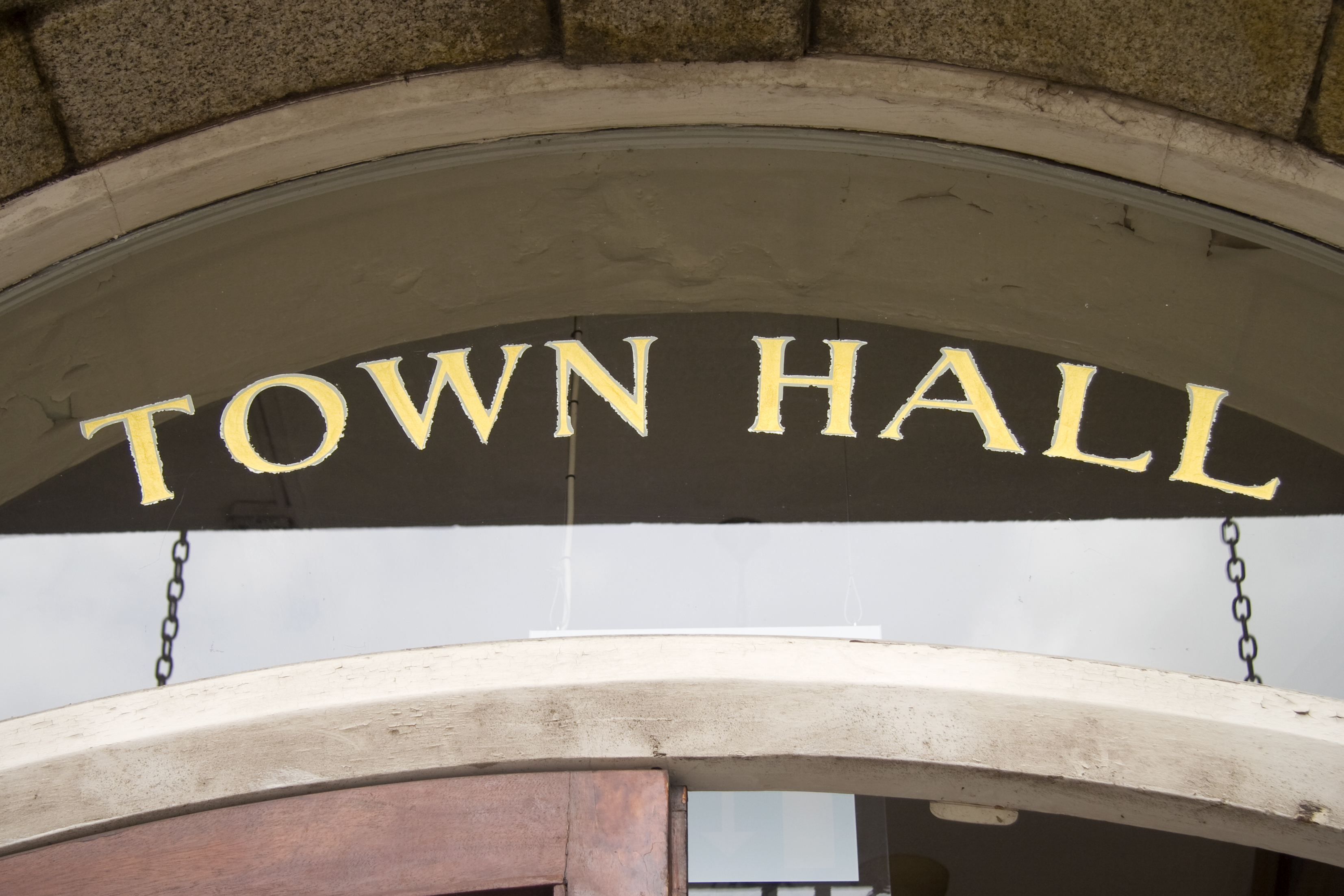 Close up of a door to a building with a glass transom above. The words "Town Hall" are stenciled on the glass in gold leaf foil.