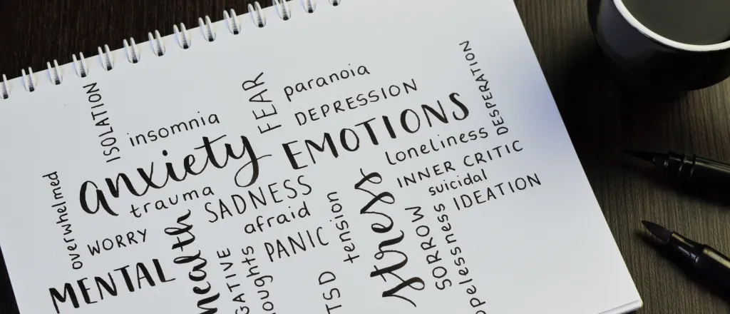 Note pad on a table with numerous descriptive words about mental health next to a cup of coffee