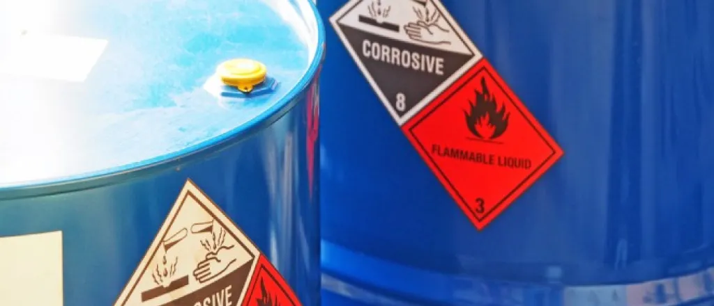 Two blue hazardous chemical barrels near each other. They both have warning labels for flammable and corrosive materials.