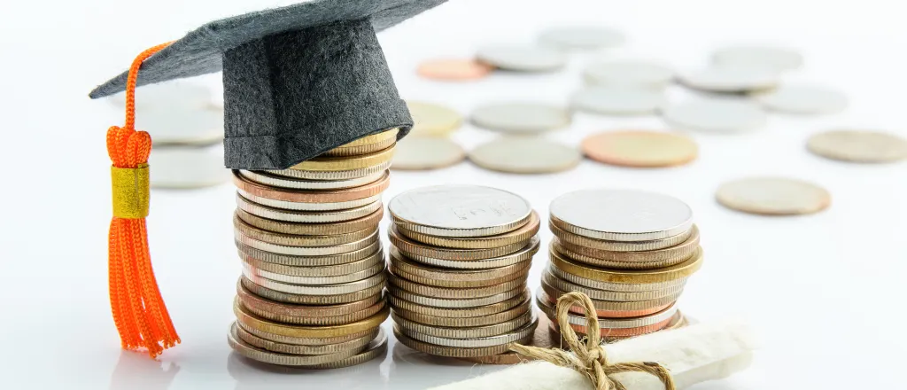 Stacks of coins with miniature mortar board on top and miniature rolled diploma in front