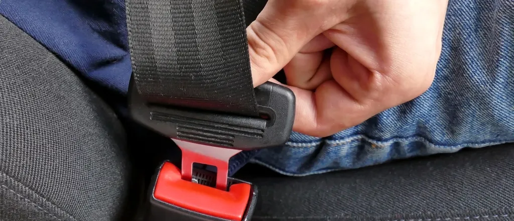 Closeup of a hand fastening a seat belt in a vehicle.