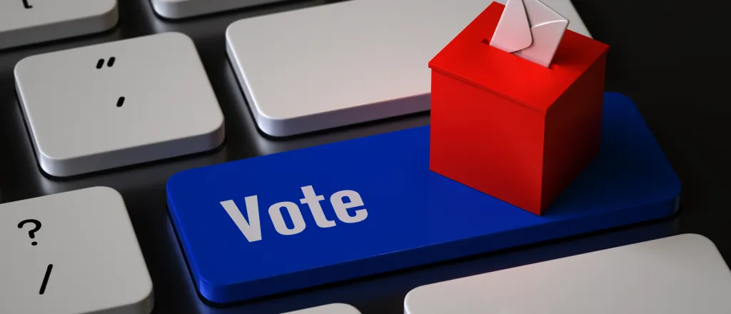 Closeup of a computer keyboard with a key labeled "Vote." A miniature ballot box is sitting on the key