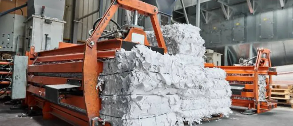 A large, orange-colored machine creates bales of shredded paper that are destined to be pulped and recycled.