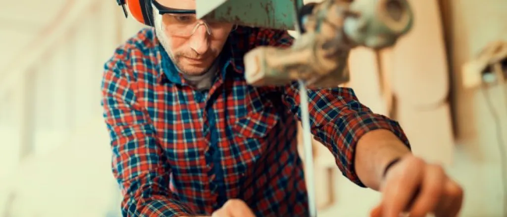 A bandsaw operator making a close cut and wearing proper safety gear such as headphones and eye protection.