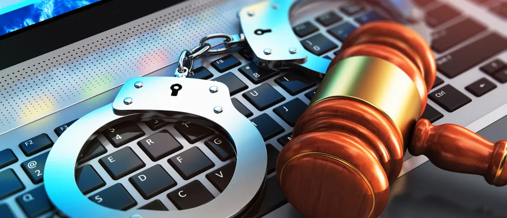 Closeup of handcuffs and court gavel on a laptop computer keyboard - scanrail - iStock-910651416