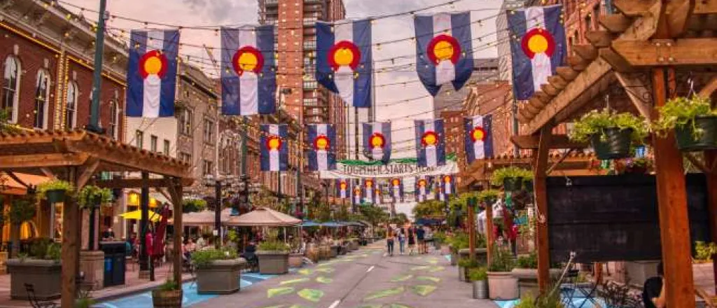 A downtown square in Colorado featuring road chalk art and hanging banners of the state flag symbol.