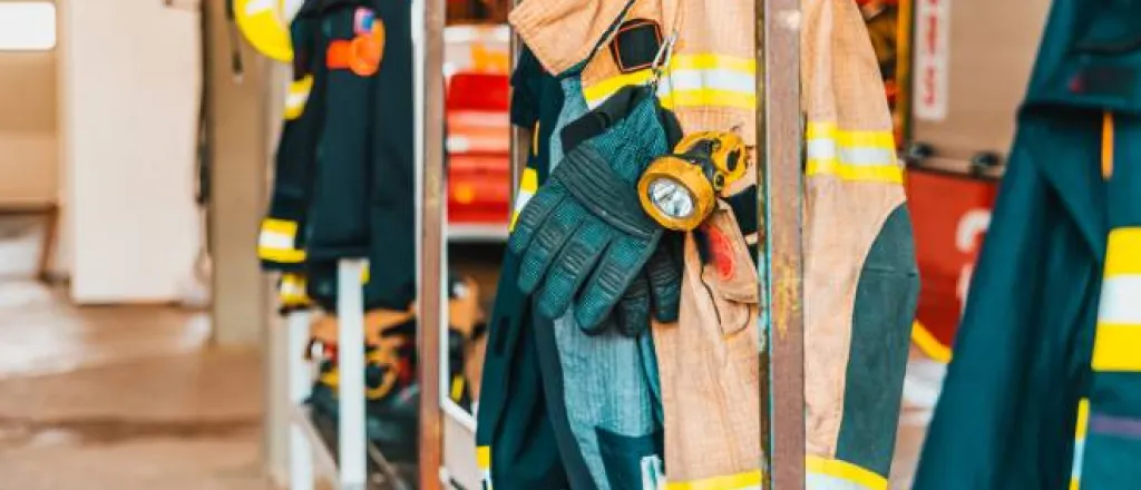 Fire-resistant clothing for firefighters, including jackets and gloves, hanging from a rusty metal rack.