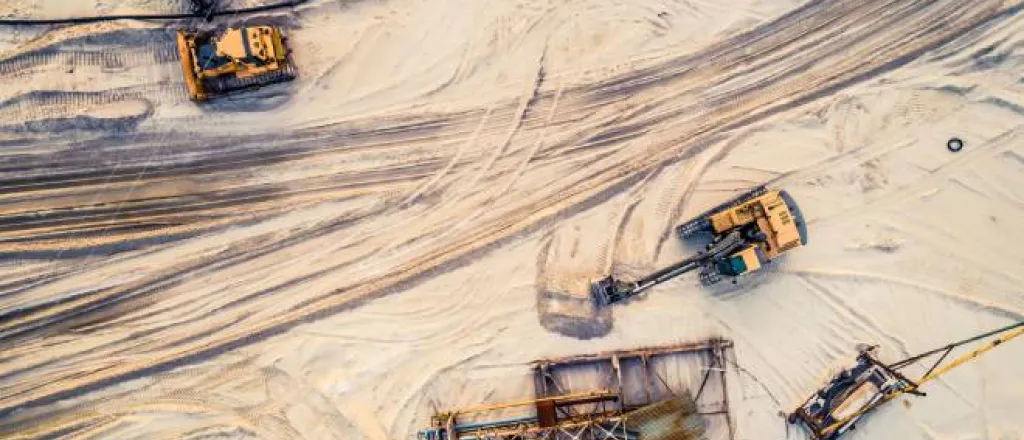 A top-down view of a sandy area with assorted industrial mining equipment sitting atop the tire-streaked sand.