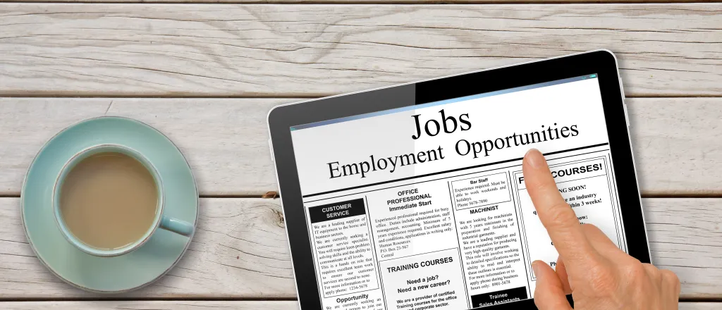 Tablet on a table next to a cup of coffee with the words "Jobs - Employment Opportunities." A hand hovers over the tablet.