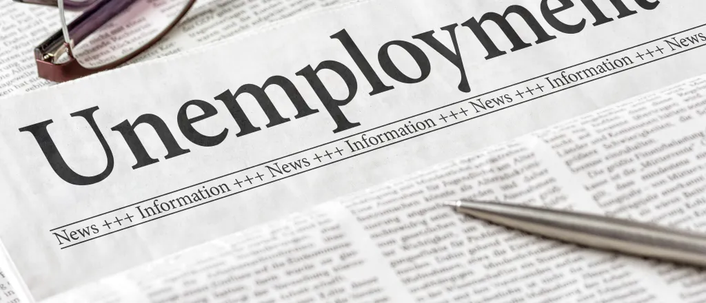 Section of a newspaper headlined "Unemployment" with a pen and pair of glasses