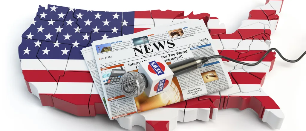 Cutout of the continental United States of America painted to resemble the national flag. A microphone rests on a newspaper on top of the cutout.