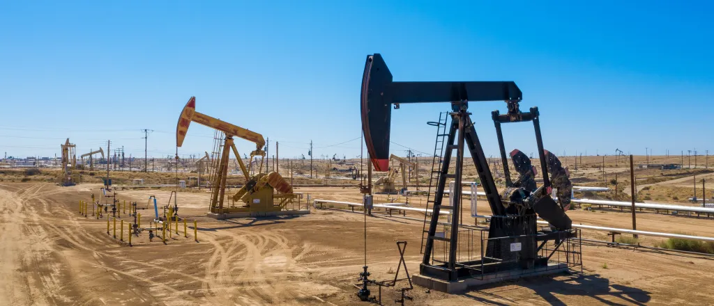 Oil pumping rigs closely spaced on bare ground under a blue cloudless sky