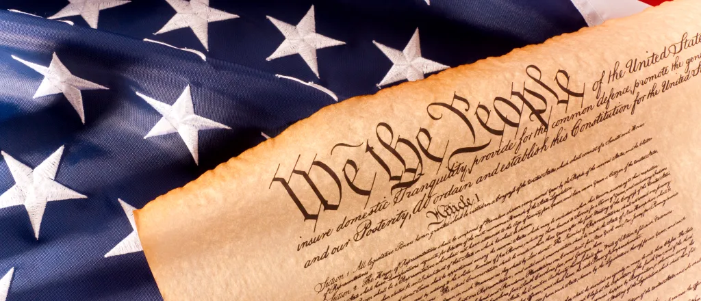 Portion of the United States constitution showing the words "We the people" on a United States flag.