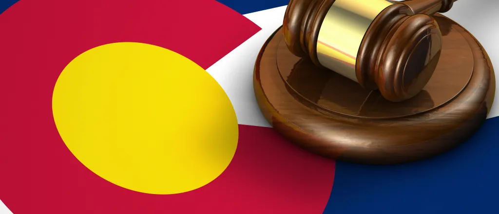 Gavel resting on a strike plate on top of a Colorado state flag.
