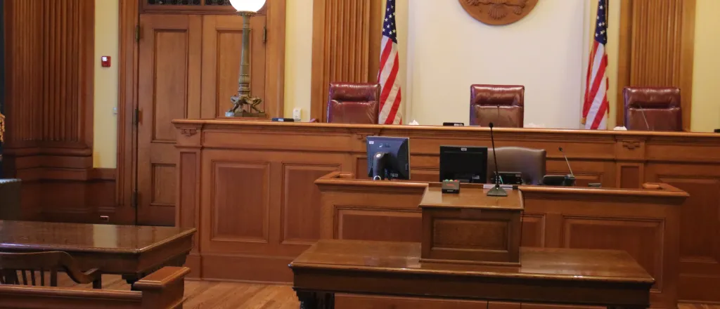 Scene of a courtroom facing the judges' bench flanked by two United States flags