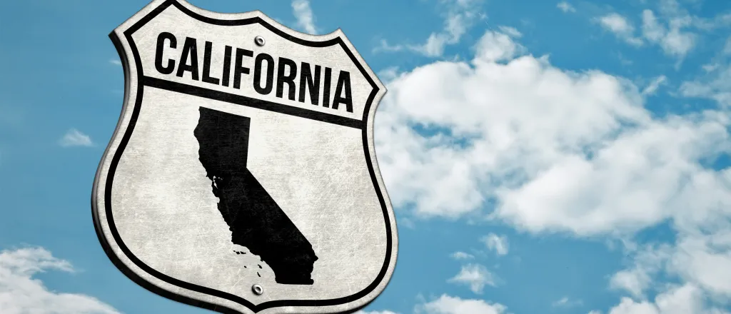 Road sign with the word "California" and a silhouette of the state. A cloudy sky is in the background.