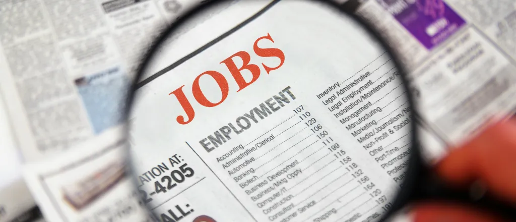 Magnifying glass over a newspaper showing the Jobs section