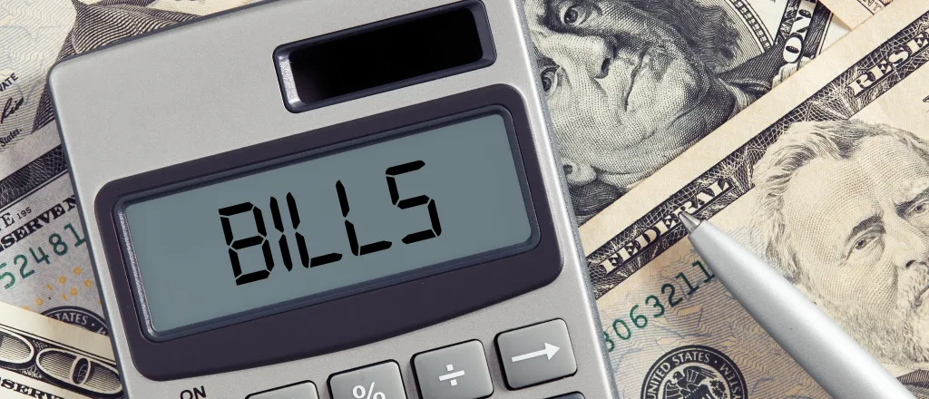 Calculator sitting on top of assorted paper money with the word "bills" displayed on the screen.