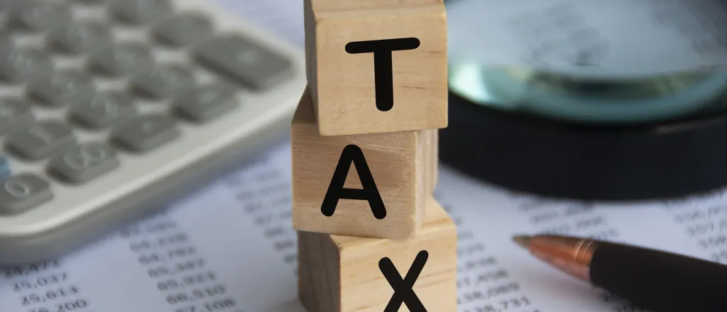 Tax word on wooden blocks with calculator, pen, magnifying glass and data analysis background.