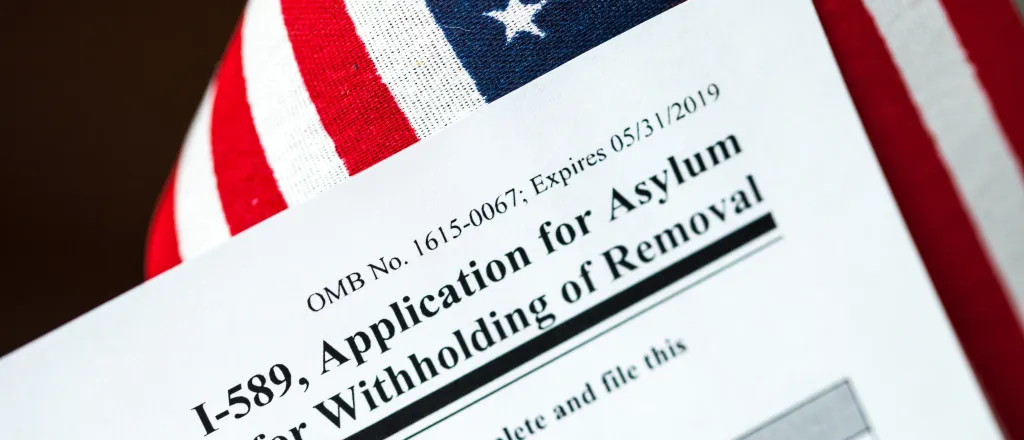 Closeup of the corner of a United States Government I-589 immigration form with a United States flag in the background.