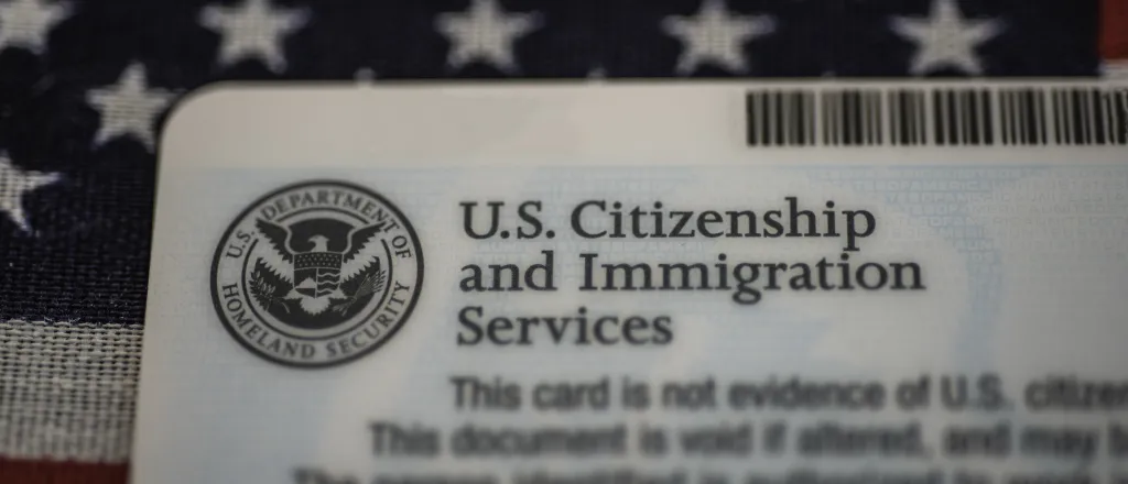 Closeup of a United States Citizenship and Immigration Services card. A United Sates flag is in the background.