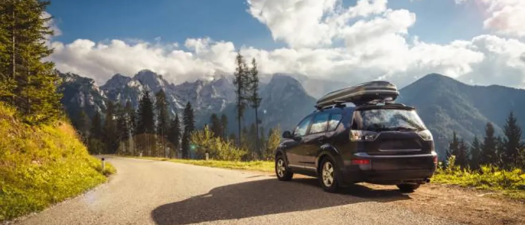A car with a hard shell roof cargo carrier parked on the side of a winding mountain road with clouds in the sky. A car with a hard shell roof cargo carrier parked on the side of a winding mountain road with clouds in the sky.