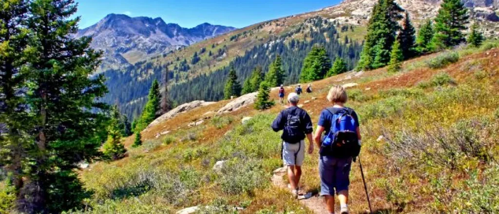 A man and woman walking through a path on Colorado's Lost Man Trail in the mountains wearing backpacks.
