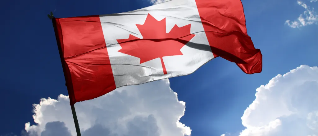 Flag of Canada against a partly cloudy, sunlit sky