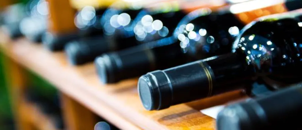 An extreme close-up view shows several dark-colored wine bottles lying on a wooden wine storage rack.