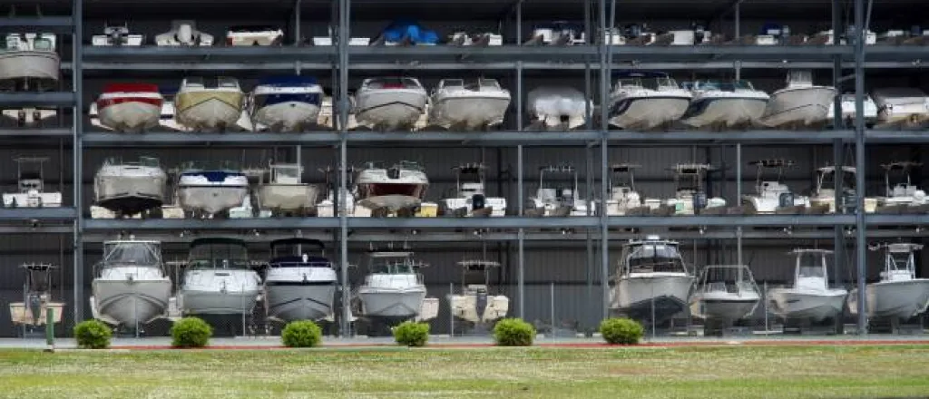 A large, open steel structure contains three shelf levels. Boats of different sizes and types sit on the various shelves.