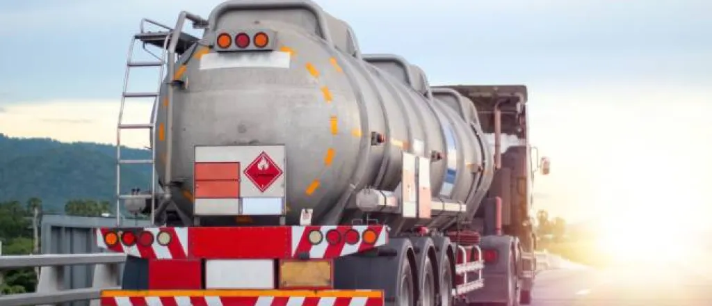 A large industrial truck driving on a road transporting flammable chemicals in a large cylindrical metal tank.