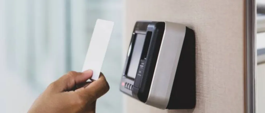 Someone standing outside a building holding a proximity key card up to the digital reader. The key card is white.