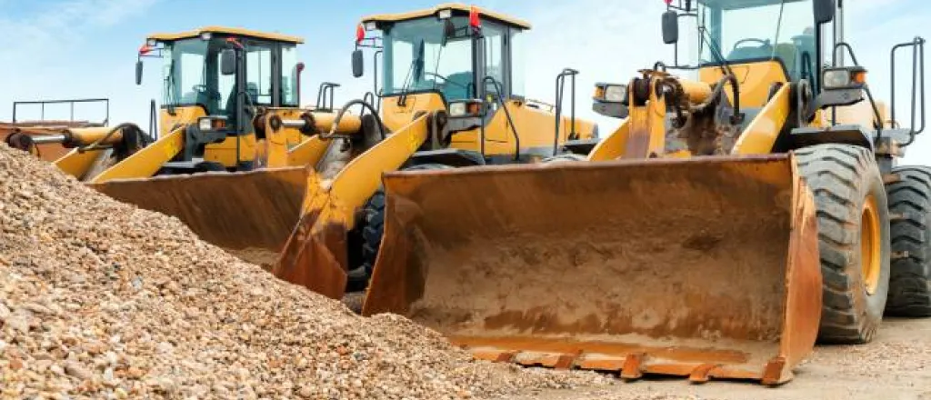 Three large orange and black excavators parked next to each other in front of a pile of rubble on a sunny day.