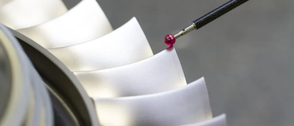 A close-up of a CMM stylus with a ruby tip taking the measurements of a part. The part has many ridges.