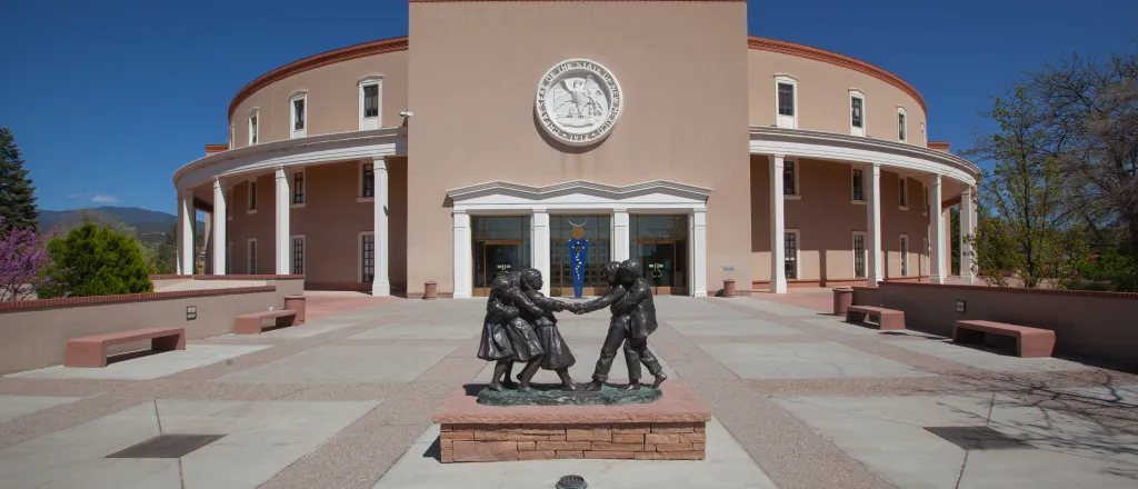PROMO HIRES Building - Government New Mexico State Capitol - jdwfoto - iStock-1487999298 Entrance to the New Mexico State Capitol building. A statue of people is in a plaza area in front of the building.