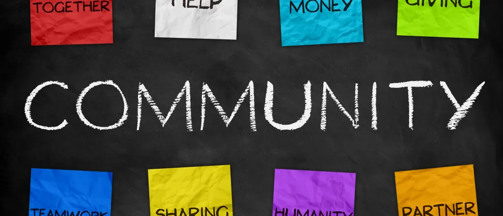 PROMO HIRES Community - Color Paper Words - iStock Word "Community" written on a chalkboard, with eight colored paper notes above and below reading "togetherness, help, money, giving, teamwork, sharing, humanity, and partner"