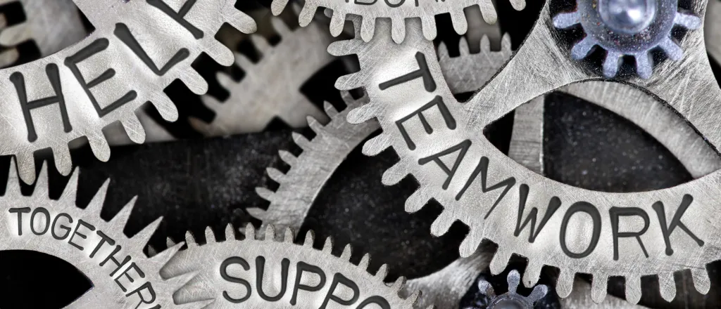Interlocking machinery gears with the words "help, collaboration, teamwork, support, and togetherness" stamped on the side