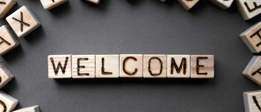 PROMO HIRES Community - Words Welcome Blocks Living - iStock - Roman Didkivskyi Assorted wooden blocks with letters on the side, surrounding wooden blocks spelling the word "welcome"