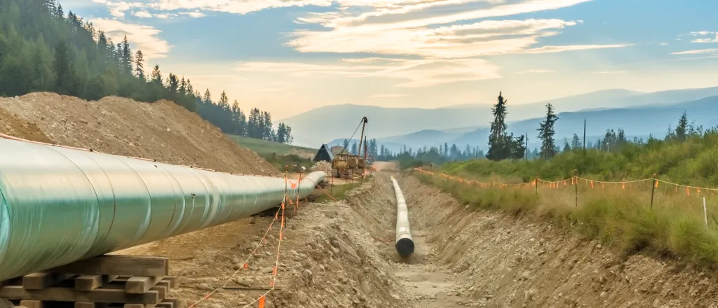 PROMO HIRES Construction Pipe Pipeline Energy - vadimgouida - iStock-1424680550 Trench in dirt with a segment of pipe, and another segment sitting above awaiting placement