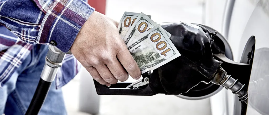 PROMO HIRES Energy - Gasoline pump fuel money cash transportation - iStock - wingedwolf Close up of a person's hand on a gas dispenser nozzle clutching three United States one hundred dollar bills.