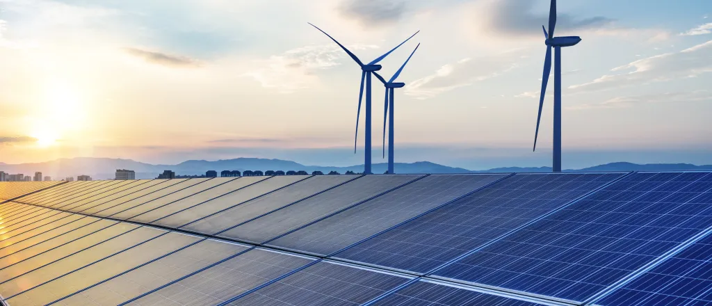 PROMO HIRES Energy - Solar Panels Wind Turbines Sky Clouds. iStock - hrul Solar panels with wind turbines in the background.