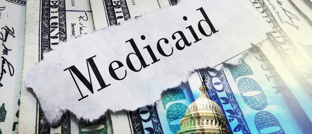 PROMO HIRES Finance - Government Medicaid Words Budget Money Cash - zimmytws - iStock-2206705589 A scrap of torn paper with the word "Medicaid" rests on top of a spread of United States 100 dollar currency.