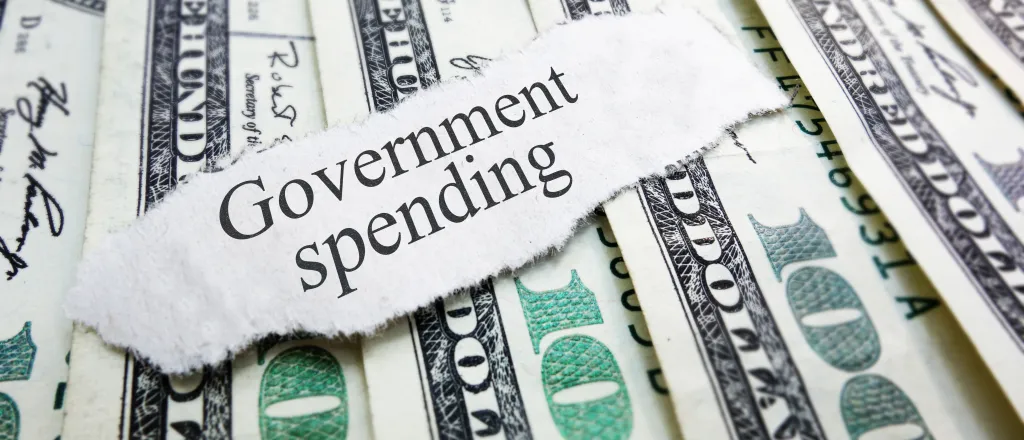 PROMO HIRES Finance - Government Spending Words Budget Money Cash - zimmytws - iStock-511889079 A scrap of torn paper with the words "Government spending" rests on top of a spread of United States 100 dollar currency.