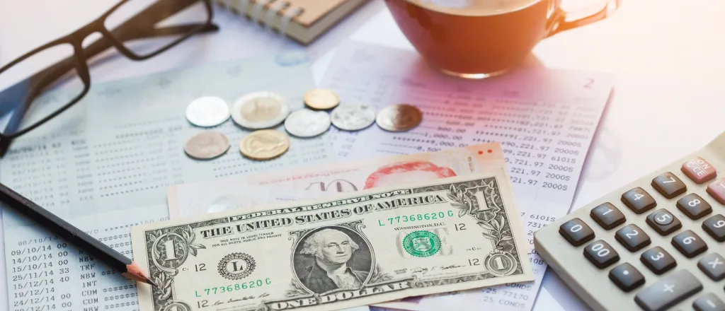 PROMO HIRES Finance - Money Dollar Calculator Glasses Statement Bank - iStock - Mamphotography Financial statement with assorted United States currency and coins, calculator, eyeglasses, and a cup of coffee on top.